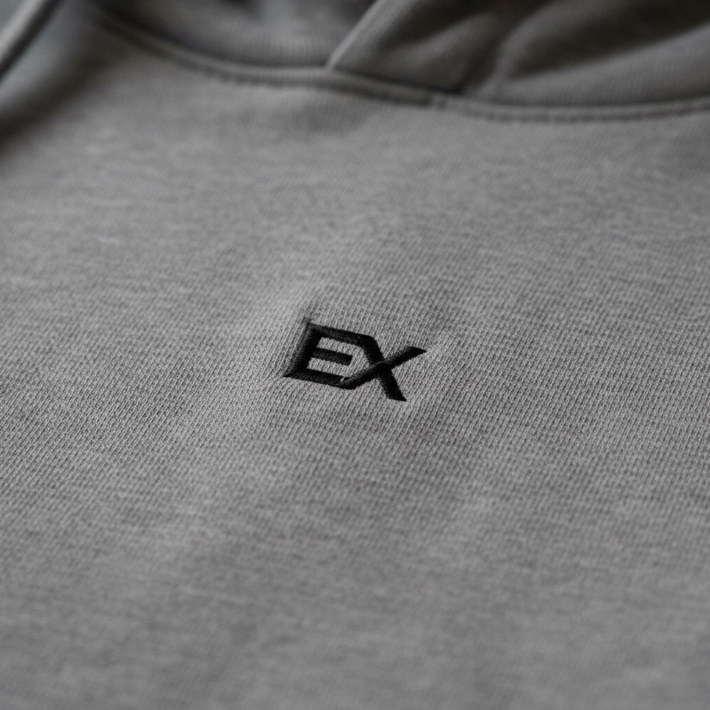 Close-up of embroidered EX monogram logo in black thread on stone grey hoodie