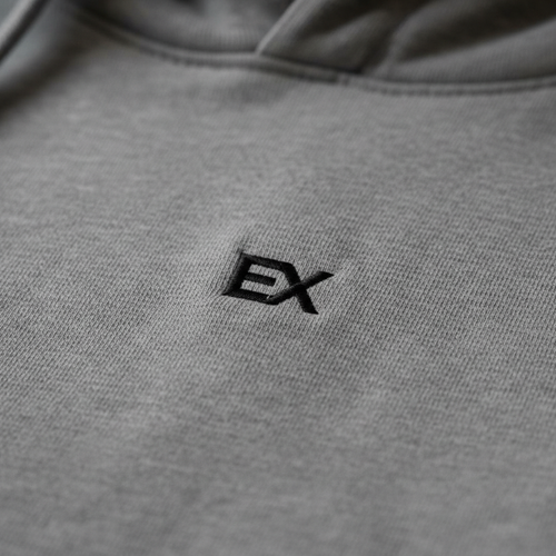 Close-up of embroidered EX monogram logo in black thread on stone grey hoodie